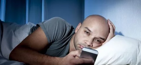jongen in bed kijkt op zijn telefoon