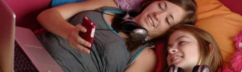 2 meisjes in bed kijkend op een telefoon